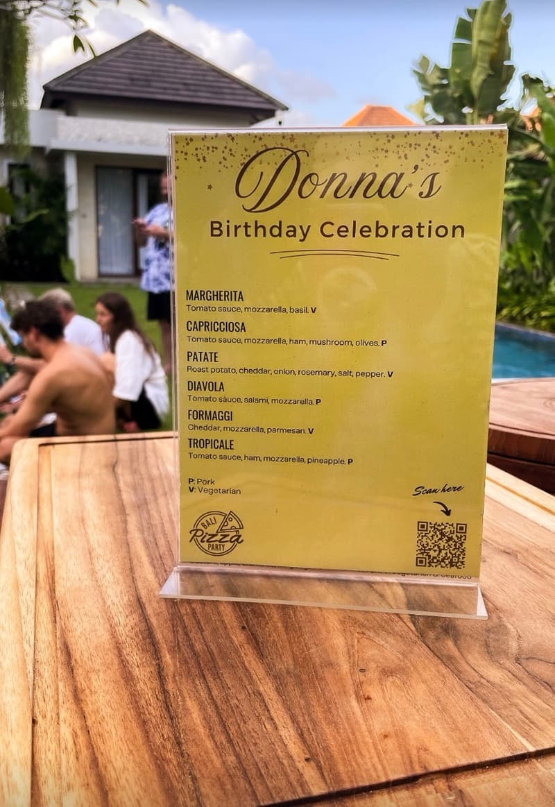 A personalised Bali Pizza Party menu card, printed for a birthday celebration and displayed poolside