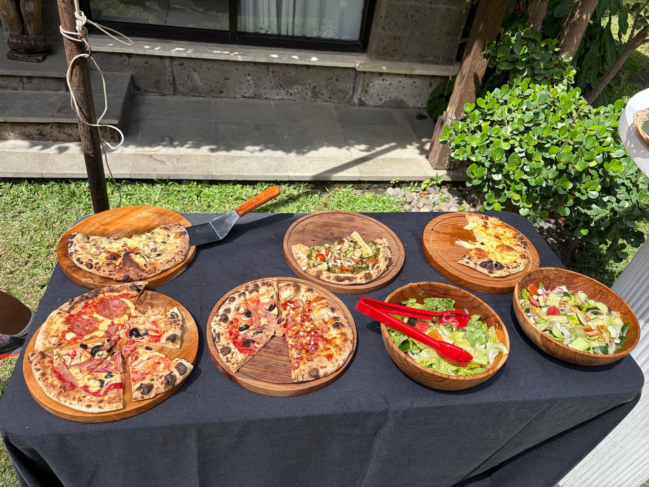 Pizzas and salads on wooden boards in the garden at Paripadi Private Villa, Canggu