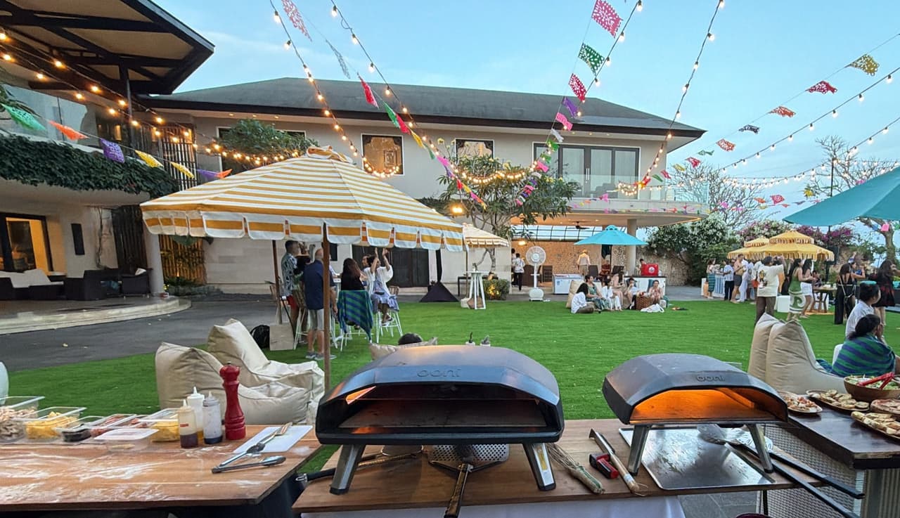 Two lit pizza ovens facing the lawn party at Pandawa Cliff Estate, string lights and bunting overhead