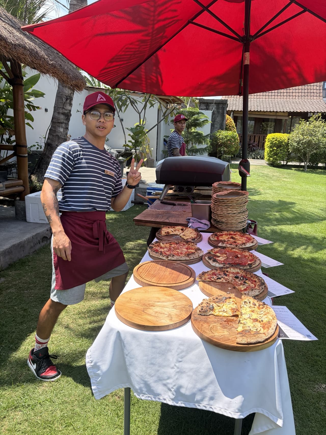 Pizzas on wooden boards under a red umbrella on the lawn at Wooden Green Paradise