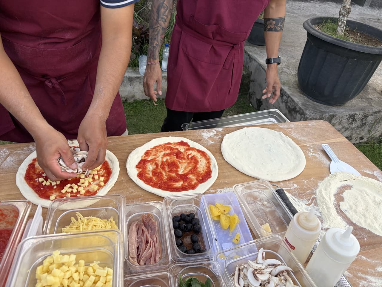 Two of our crew topping pizzas at the prep station